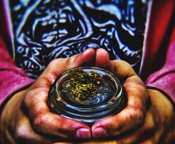 Midsection of man holding marijuana joint in container