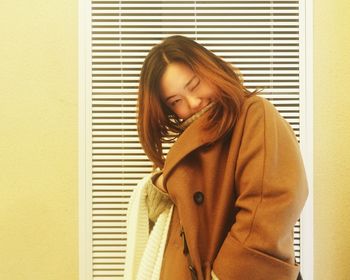 Portrait of young woman wearing jacket standing against wall