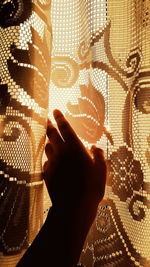 Cropped hand touching curtain during sunset