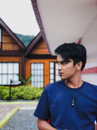 Young man looking away while standing against building