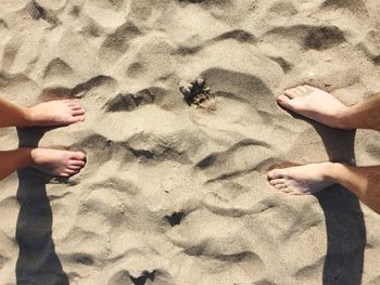 Low section of people standing at sandy beach on sunny day