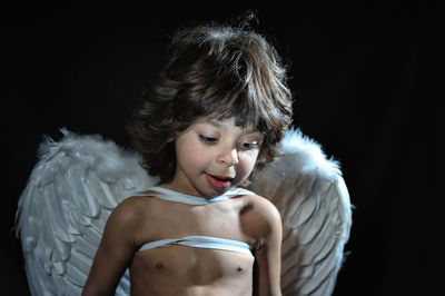 Close-up of boy wearing angel wings against black background