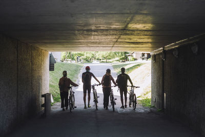 Male and female friends wheeling with cycles while walking through underpass