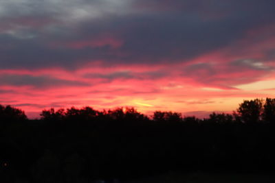 Silhouette trees against dramatic sky during sunset