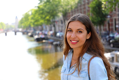 Portrait of young woman standing by canal in city