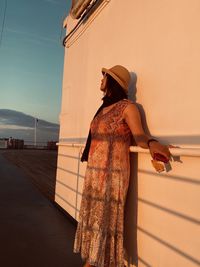 Woman standing against wall and sky during sunset