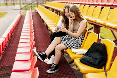 Two friends of a schoolgirl or a student are sitting in the stands and watching videos 