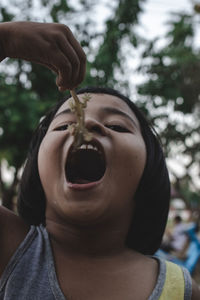 Low angle portrait of girl eating lizard while standing outdoors