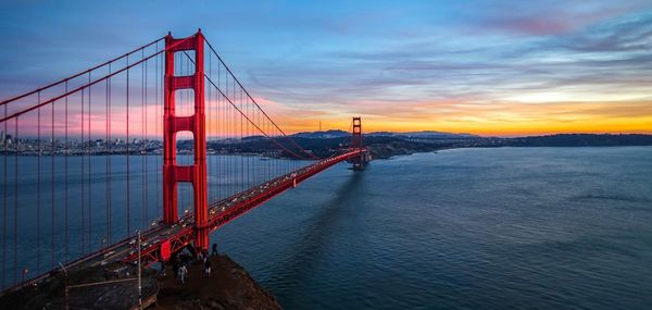 Suspension bridge over sea against cloudy sky