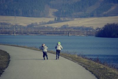 Rear view of sibling roller skating on footbath by river