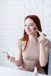 Woman holding make-up brushes and making up with cosmetics set at home