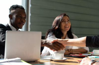 Business persons shaking hands while sitting in office