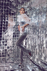 Space fashionable brunette woman in silver clothes stands against the background of a silver wall