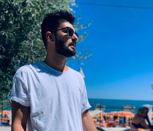 Young man wearing sunglasses standing against sea