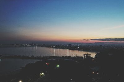 Illuminated city by sea against sky during sunset