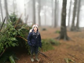 Tilt-shift portrait of smiling girl standing at forest during foggy weather