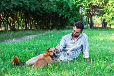 Handsome smiling man sitting on grass with his dog in park. concept of human and pet relationship.