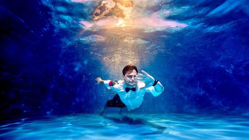 Full length of man carrying red rose in mouth while swimming in pool