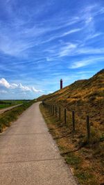 Footpath amidst field against blue sky