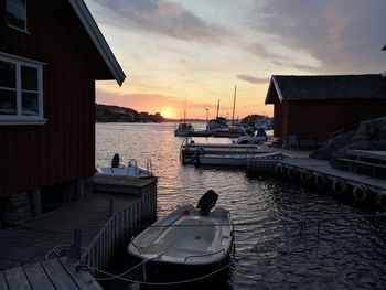 Boats moored on sea by buildings against sky during sunset