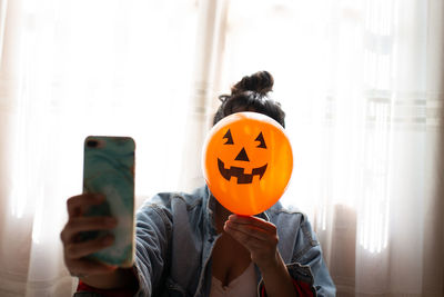 Close-up of woman holding halloween decoration against face and taking selfie at home