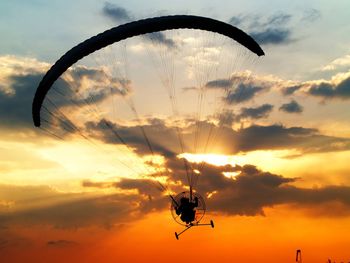 Silhouette man paragliding against sky during sunset