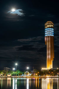 Illuminated roi et tower by river against sky at night