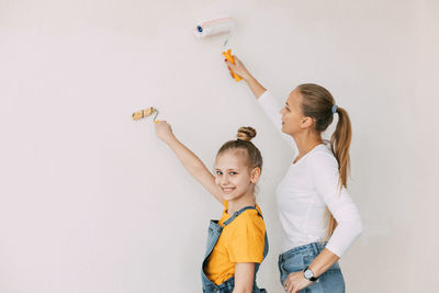 Beautiful and happy mom and daughter paint the walls in the apartment white.