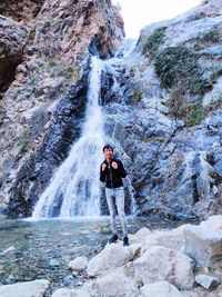 Full length of boy standing on rock against waterfall