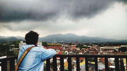 Rear view of man looking at cityscape against sky