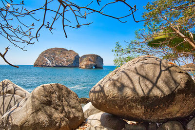 Rocks by sea against clear blue sky