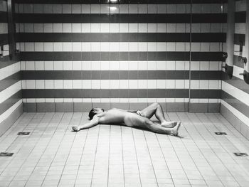 Naked man lying on tiled floor at home