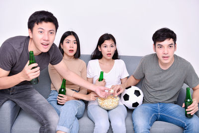 Friends watching sports while sitting on sofa against wall