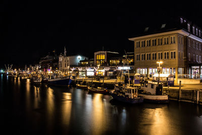 Boats moored at harbor against houses at night