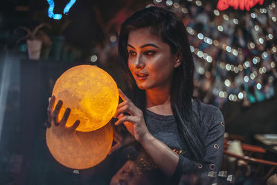 Portrait of young woman holding illuminated lighting equipment at night