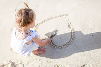 High angle view of girl making heart shape on sand at beach