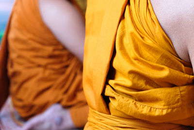 Midsection of monks wearing traditional clothing while sitting in temple