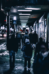 Rear view of people walking on sidewalk at night