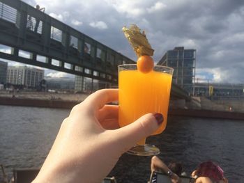 Close-up of hand holding drink by river against sky