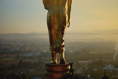 Statue of budda against buildings in city at sunset