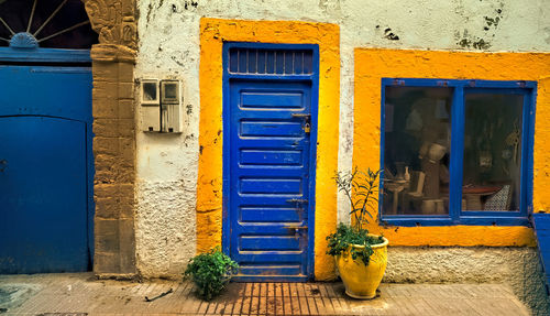 Old facade of a house with yellow framed window and door, both blue. lamp above the door.