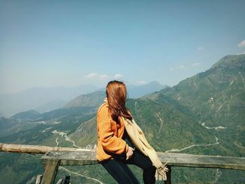 Woman looking at mountain while sitting on railing
