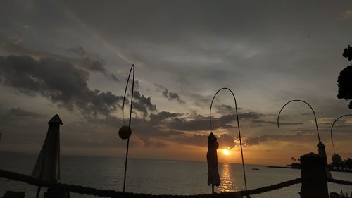 Silhouette street by sea against sky during sunset