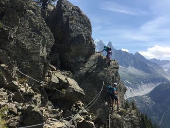 People climbing on rock against sky