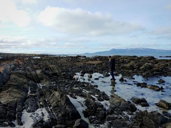 Man standing on rock by sea against sky