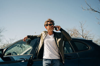 Man wearing sunglasses standing by car against sky