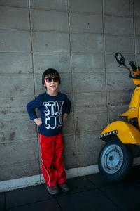 Full length of boy standing by motor scooter against wall