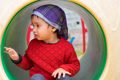 Cute girl looking away while sitting on outdoor play equipment