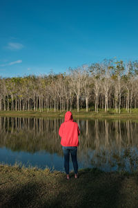 Rear view of woman in hood clothing by lake against sky