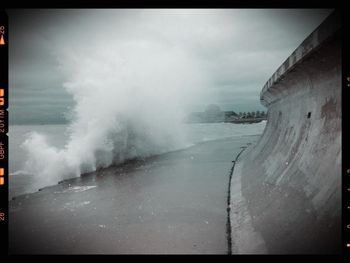 Waves splashing on rocks against cloudy sky